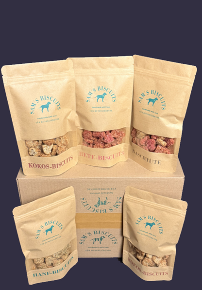 Fünf Tüten Hundekekse vor einem Versandkarton mit den besten leckerlies für Hunde