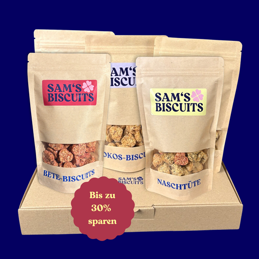 Fünf Tüten besonderer Hundeleckerlis von SAM'S BISCUITS auf einem Karton, ein roter Sticker signalisiert in diesem Angebot kannst du bis zu 30% sparen